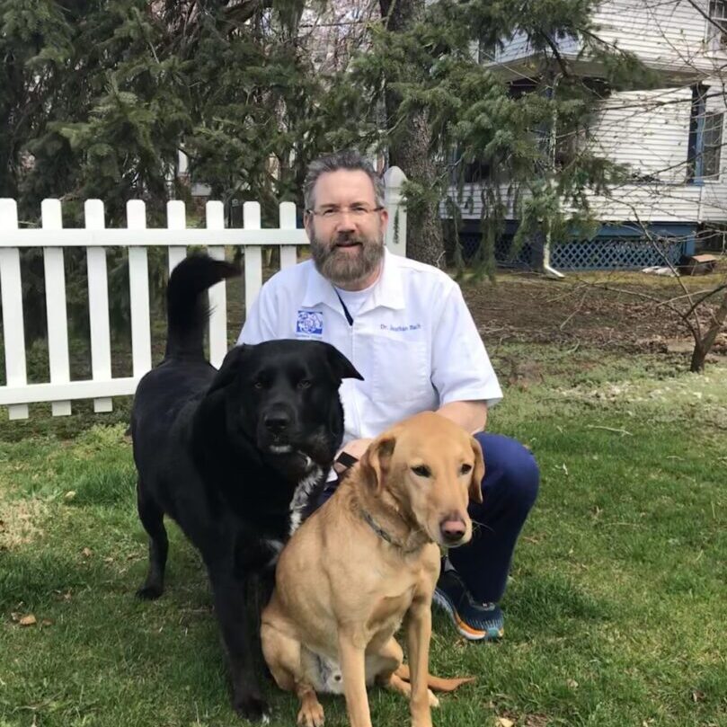 A man sitting on the grass with two dogs.